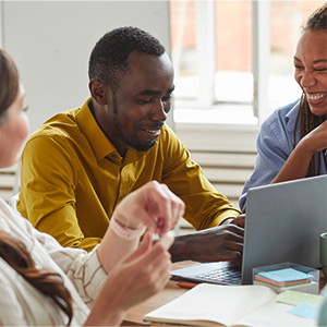 Photo of three people sitting around a laptop