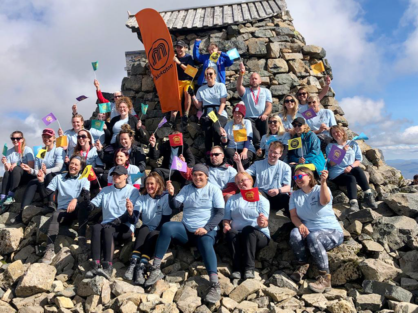 A group of hikers at the summit of Snowdon, waving Makaton flags
